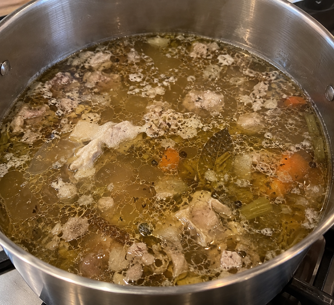 Grote pan met zelfgemaakte bottenbouillon die zacht staat te trekken op het fornuis